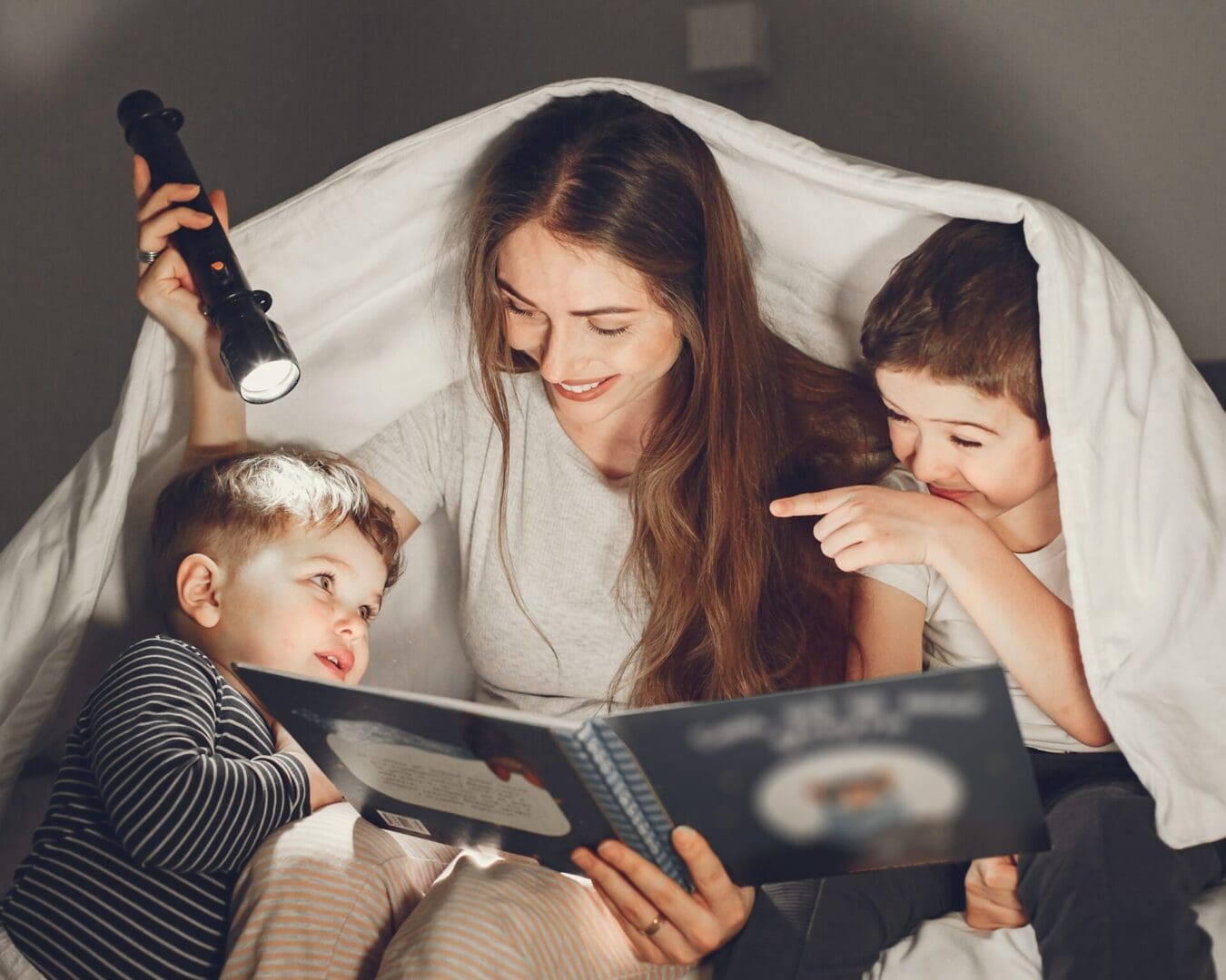 An author is reading a children's book to her young ones under a cozy blanket, bringing a fresh perspective to their storytelling time.